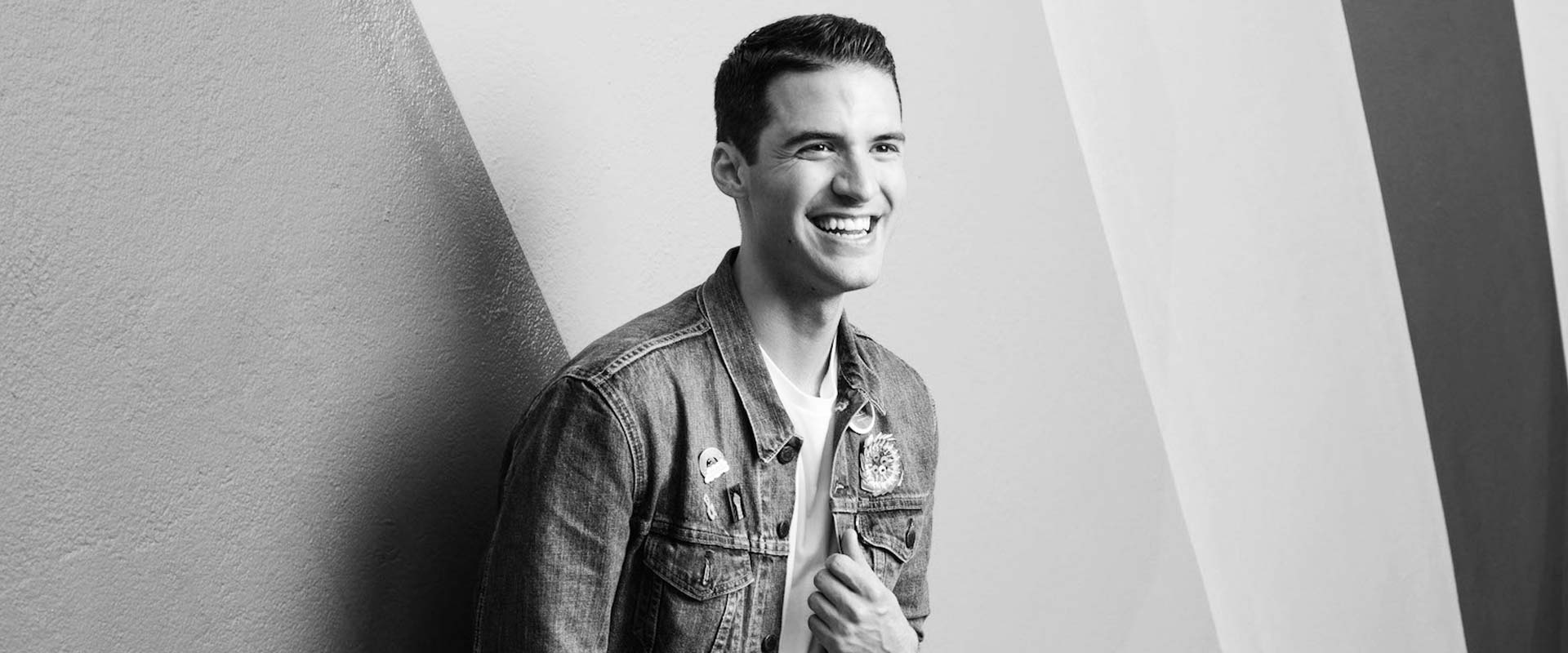 Beautiful gay guy smiling leaning against a rainbow-coloured wall